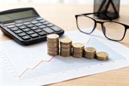 Bureau avec courbe ascendante, calculatrice, lunettes et piles de pièces en euros croissantes